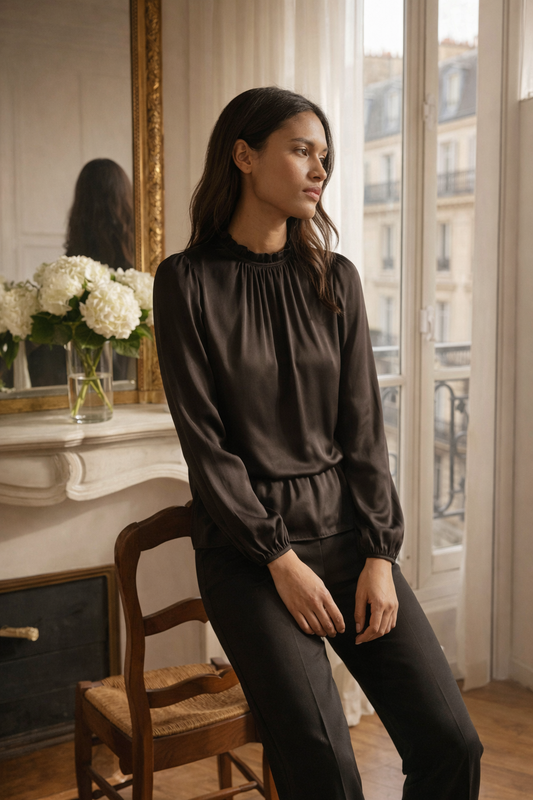 Black long-sleeve blouse with a softly gathered neckline and relaxed drape styled in a light-filled interior.