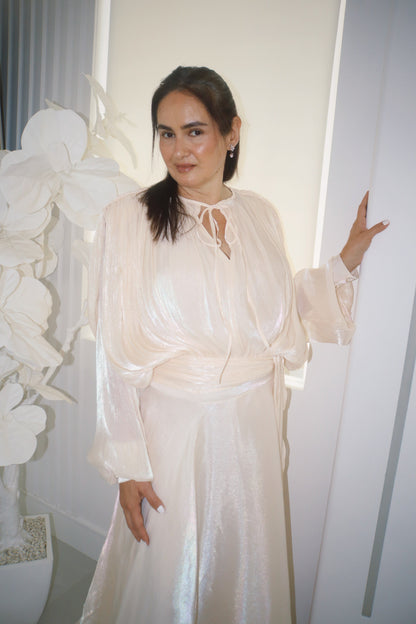 Woman in a pearly white dress standing indoors with decorative elements.
