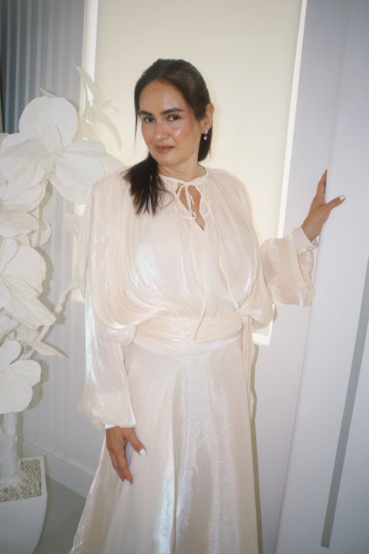 Woman in a pearly white dress standing indoors with decorative elements.