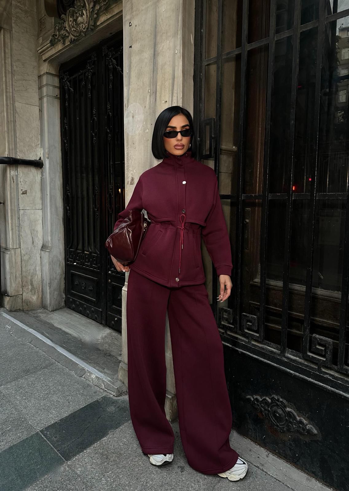 Model wearing a burgundy lounge set with cinched-waist jacket and wide-leg pants styled for an elevated street look.